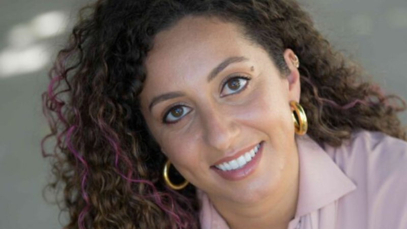 Headshot of Rabbi Tarlan Rabizadeh in a purple shirt, gold earrings, and purple streaks in her hair