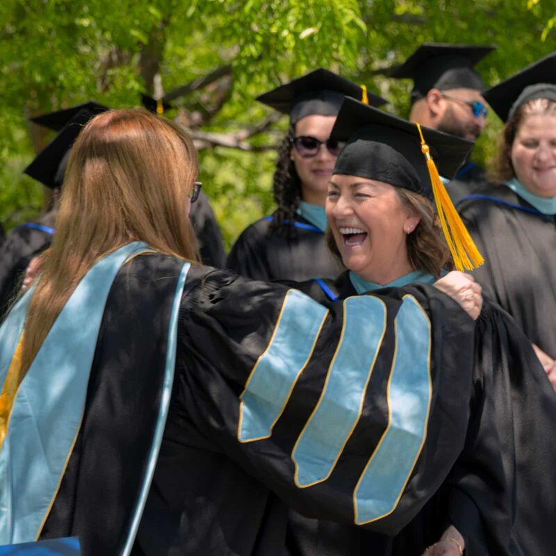 Graduates in caps and gowns smiling and embracing outdoors at the Masor School for Jewish Education & Leadership.