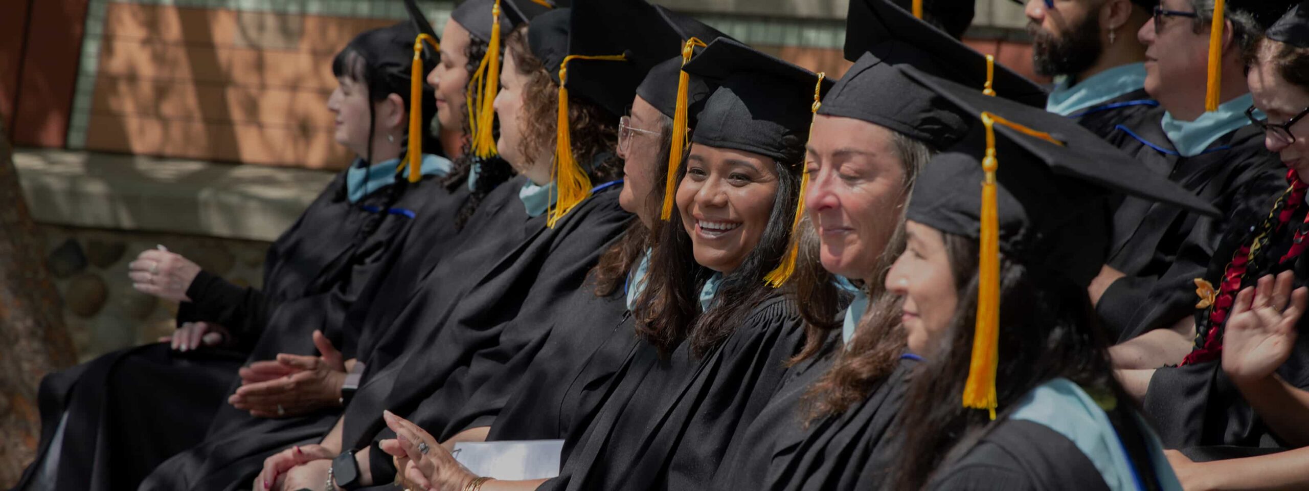 Graduates in caps and gowns seated together and smiling during a ceremony at the Masor School for Jewish Education & Leadership.