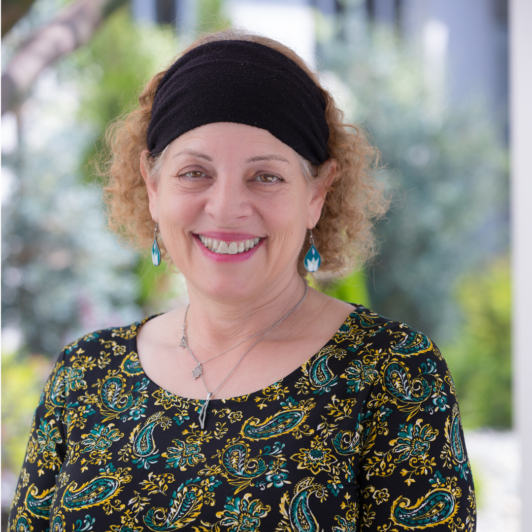 headshot of Sari Abrams in a black headband and paisley shirt