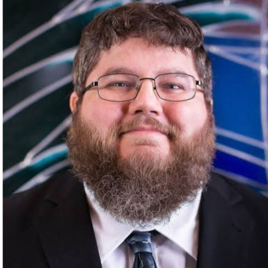Headshot of Rabbi Brodie in a black suit jacket, white collared shirt, and blue tie, with classes on