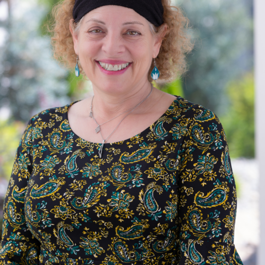 Headshot of Sari Abrams in black headband and patterned shirt