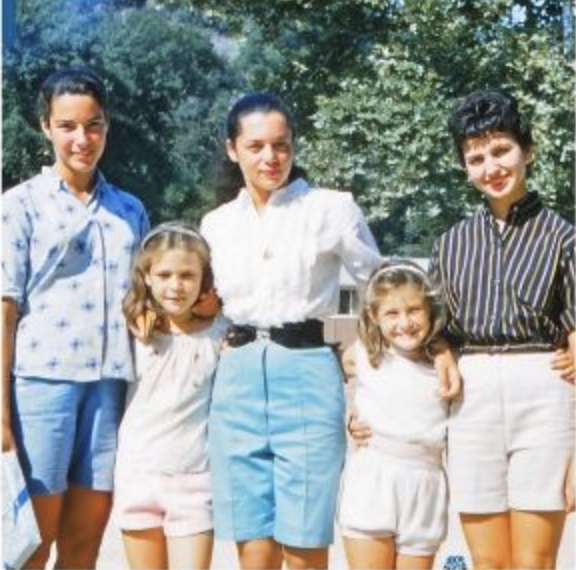 A vintage photo of 3 women and 2 girls with their arms around each other outside.