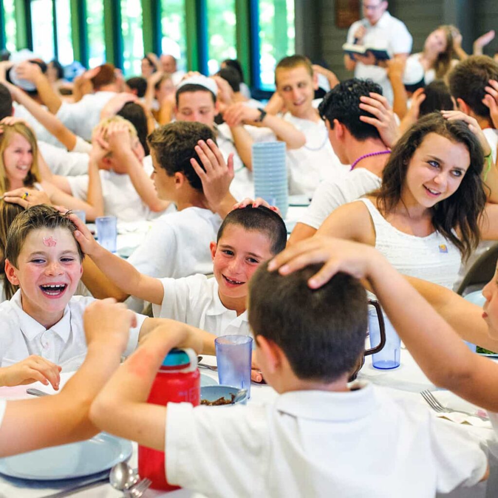 Campers laughing and eating together in a dining hall at a Jewish summer camp.