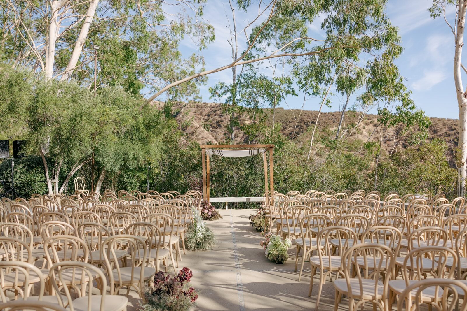 A Chuppah and chairs are set up outside on a terrace with trees in the background—prepped for a wedding.