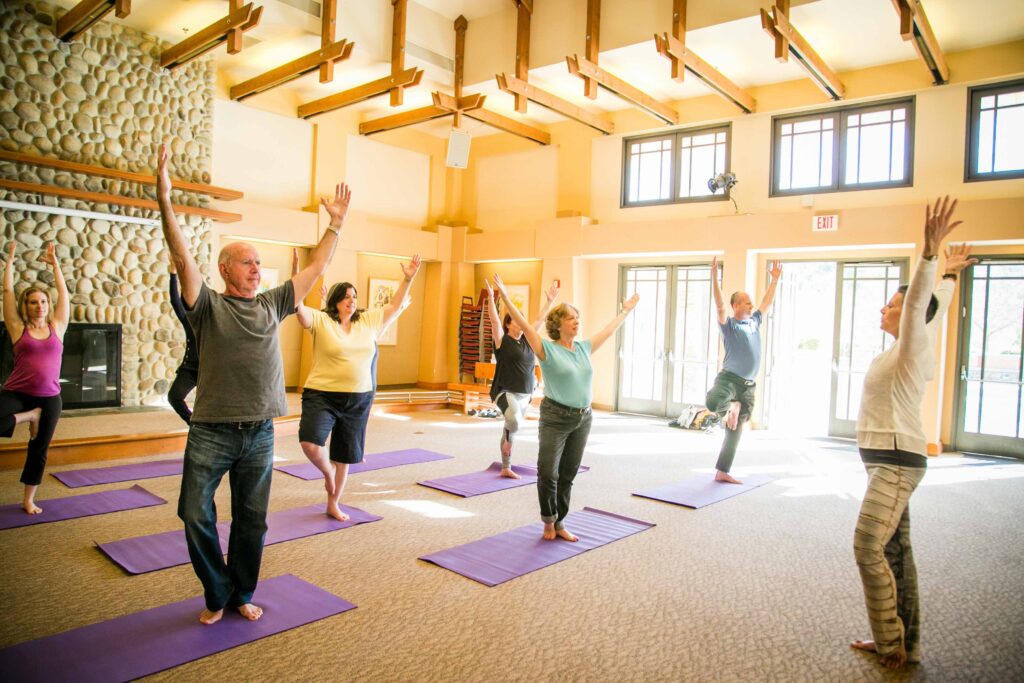 Several people in a well-lit room doing a yoga pose with a fireplace in the background.