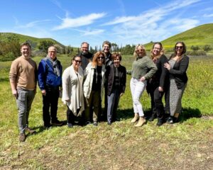 A group of people outside on a hill, smiling at the camera on a bright, sunny day.