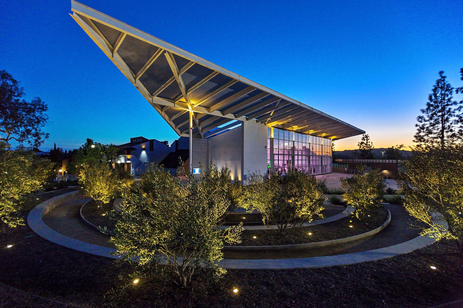 A photo of Stephen Wise Temple—a beautiful architectural structure with a triangular roof overhang with circular concrete plant beds in front and set against a sunset.