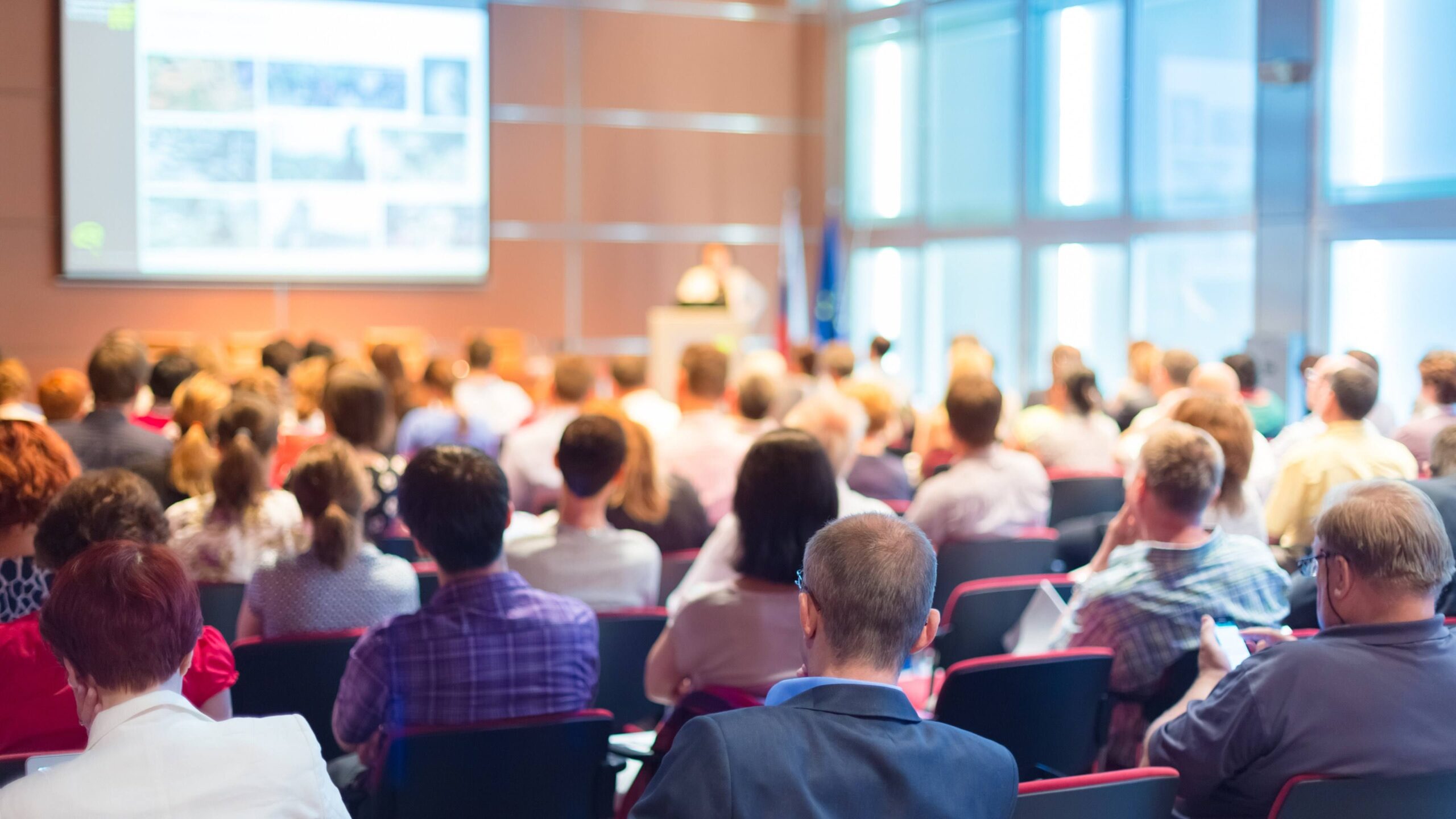 At the back of a large conference room with people in chairs and a speaker at the front.