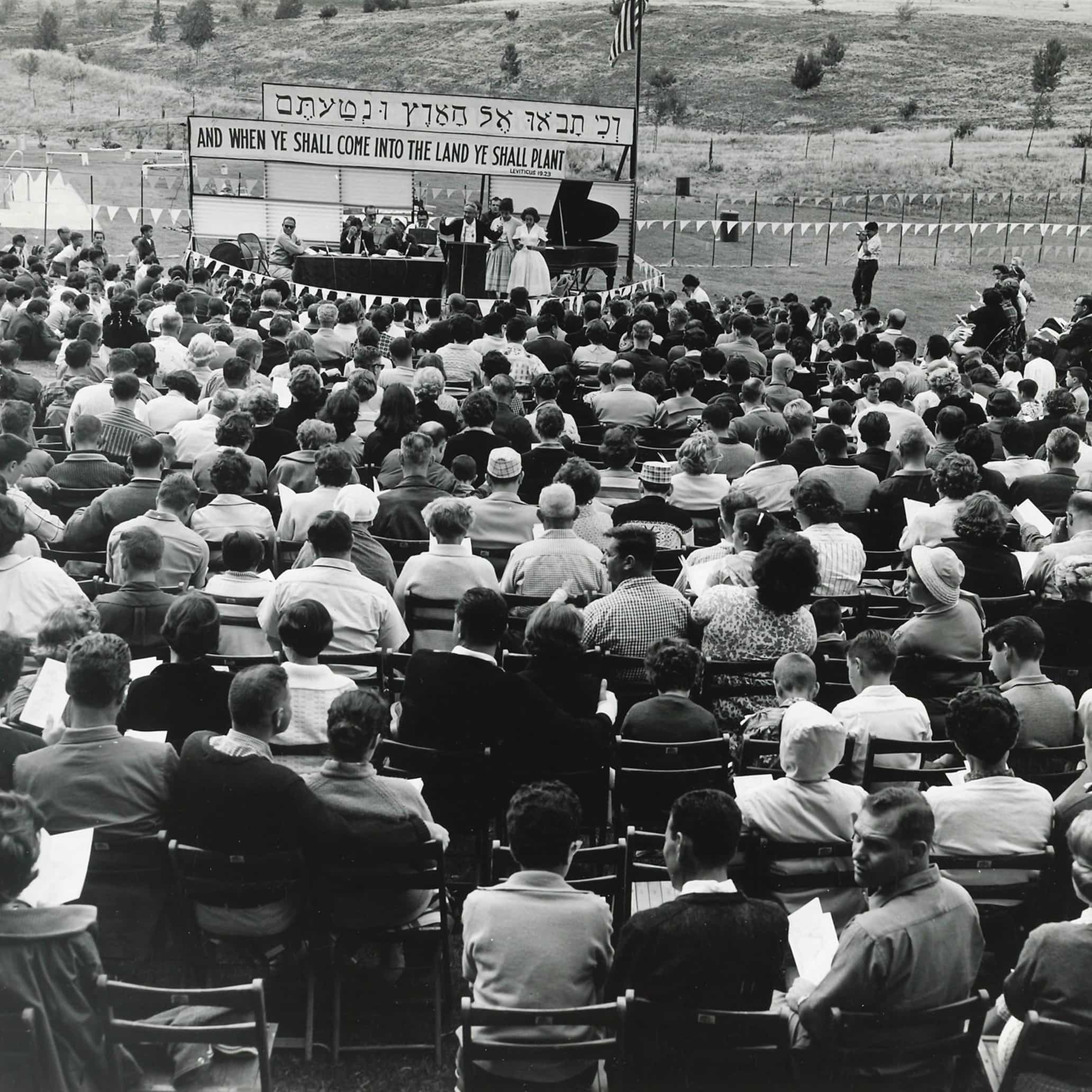 Archival photo of a group of people on a lawn watching a performance in black and white.