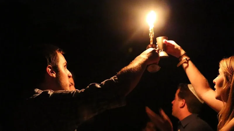 Two people light a havdalah candle in the dark