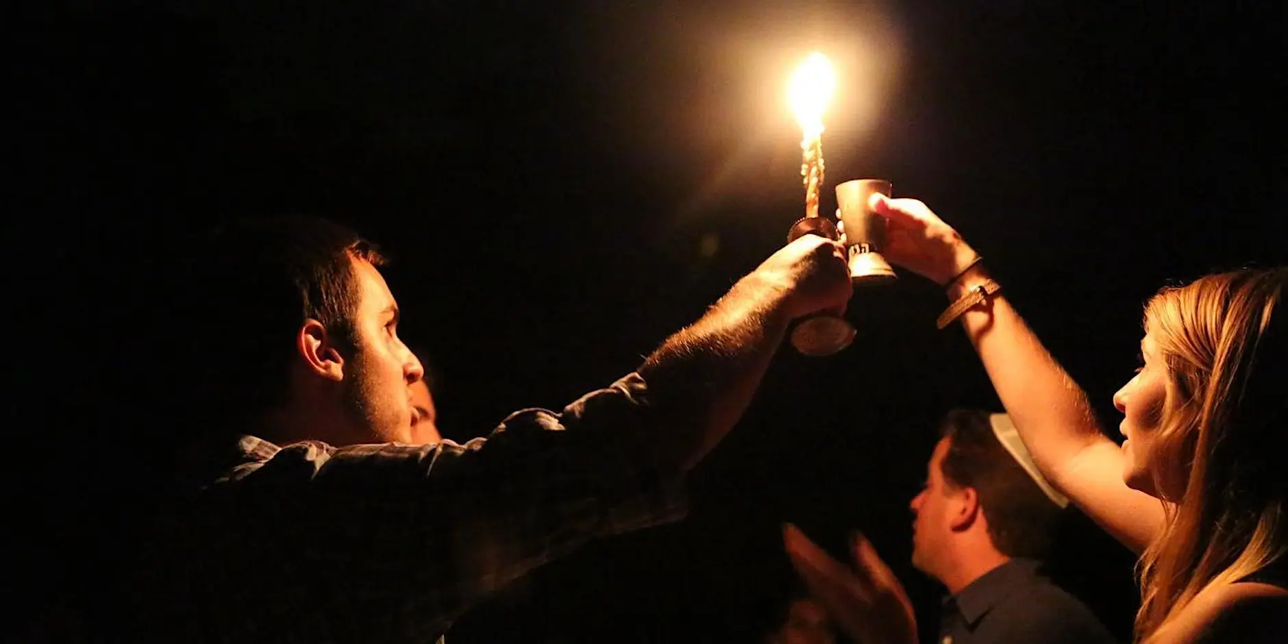 Two people light a havdalah candle in the dark