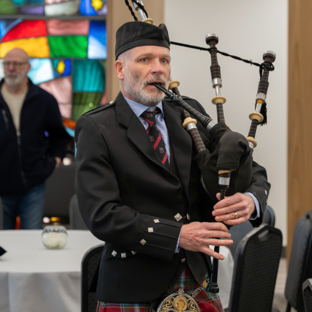Kevin McIntyre in a suit and kippah playing bagpipes in a synagogue