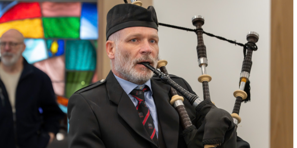 Kevin McIntyre in a black suit and black kippah playing the bagpipes in a synagogue with stained glass windows
