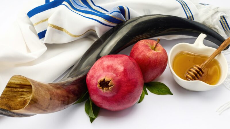 A tallis, shofar, bowl of honey, red apple, and a pomegranate