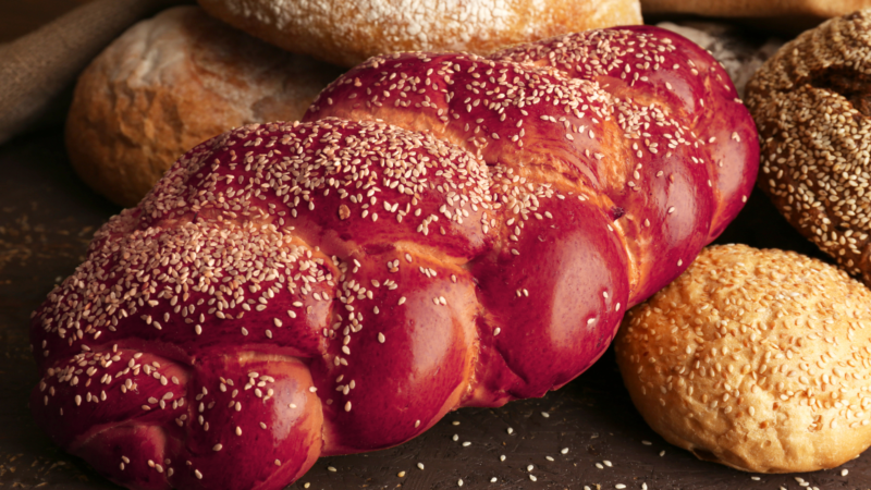 photo of a large pink challah next to other loaves of bread