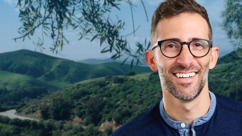 Ari Bloom in black glasses and a blue shirt against the BBC backdrop