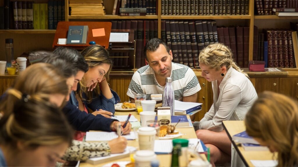 8 people sitting around a table in a library studying