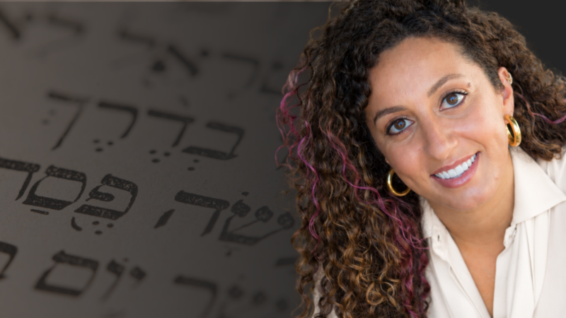 Rabbi Tarlan Rabizadeh in a white shirt and gold earrings against a background with Hebrew letters