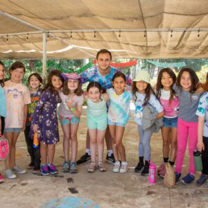 A counselor poses under a canopy with a group of campers