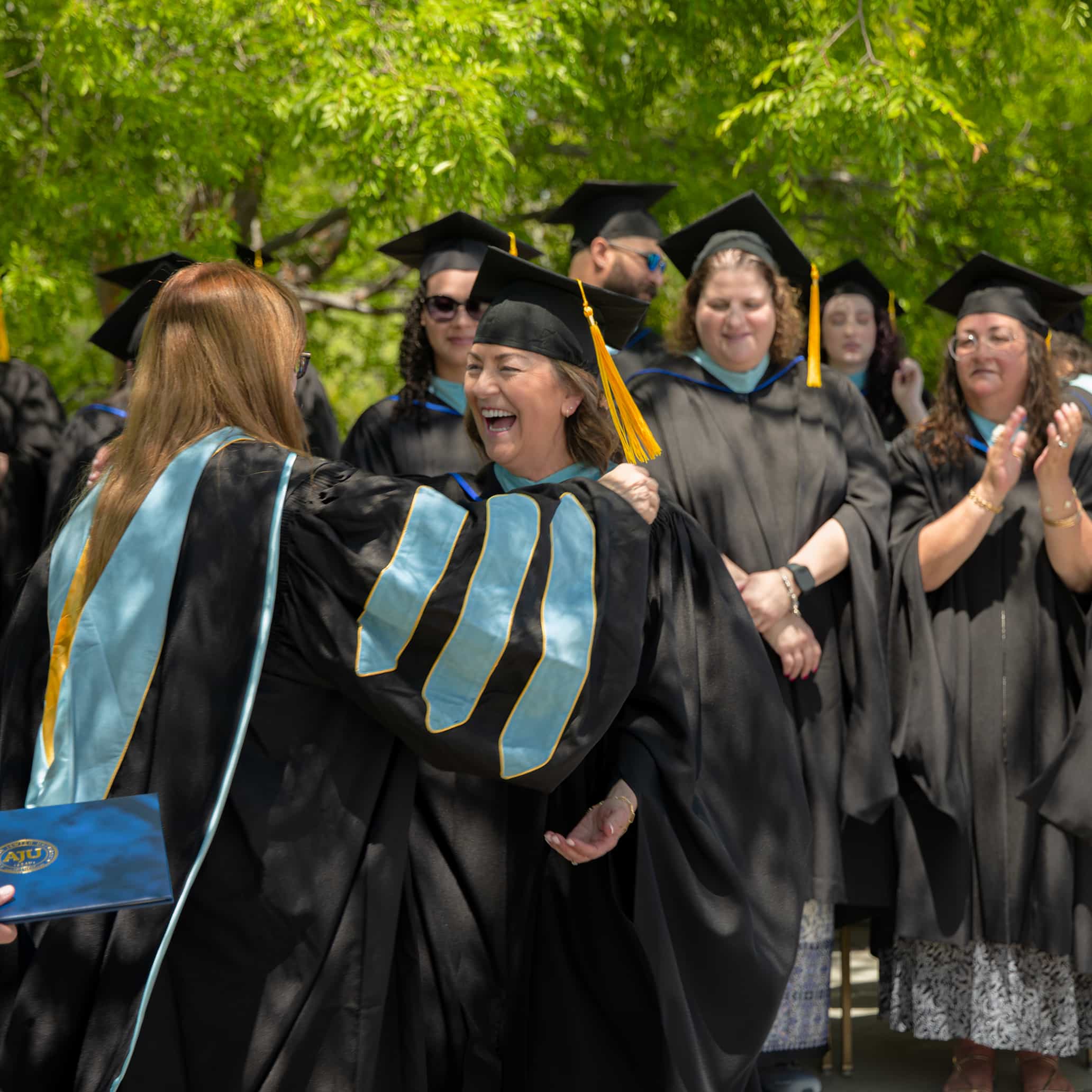 Masor EdD graduates in cap and gown hug at graduation