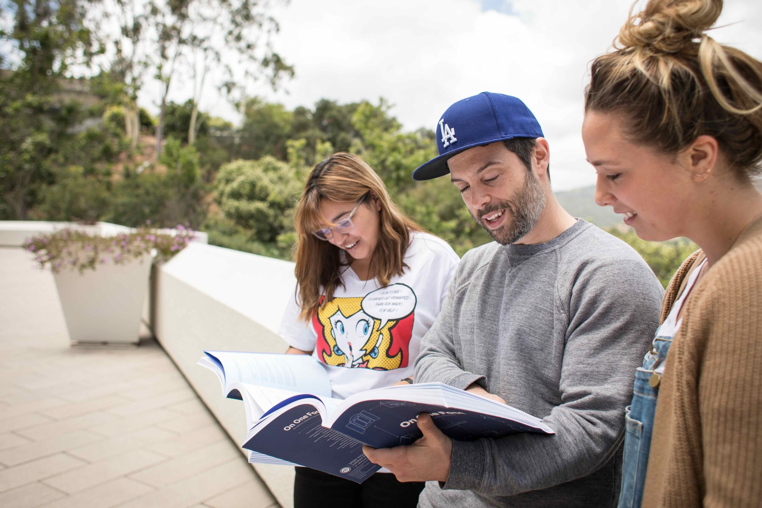 3 people outside on a school patio looking at a book together.