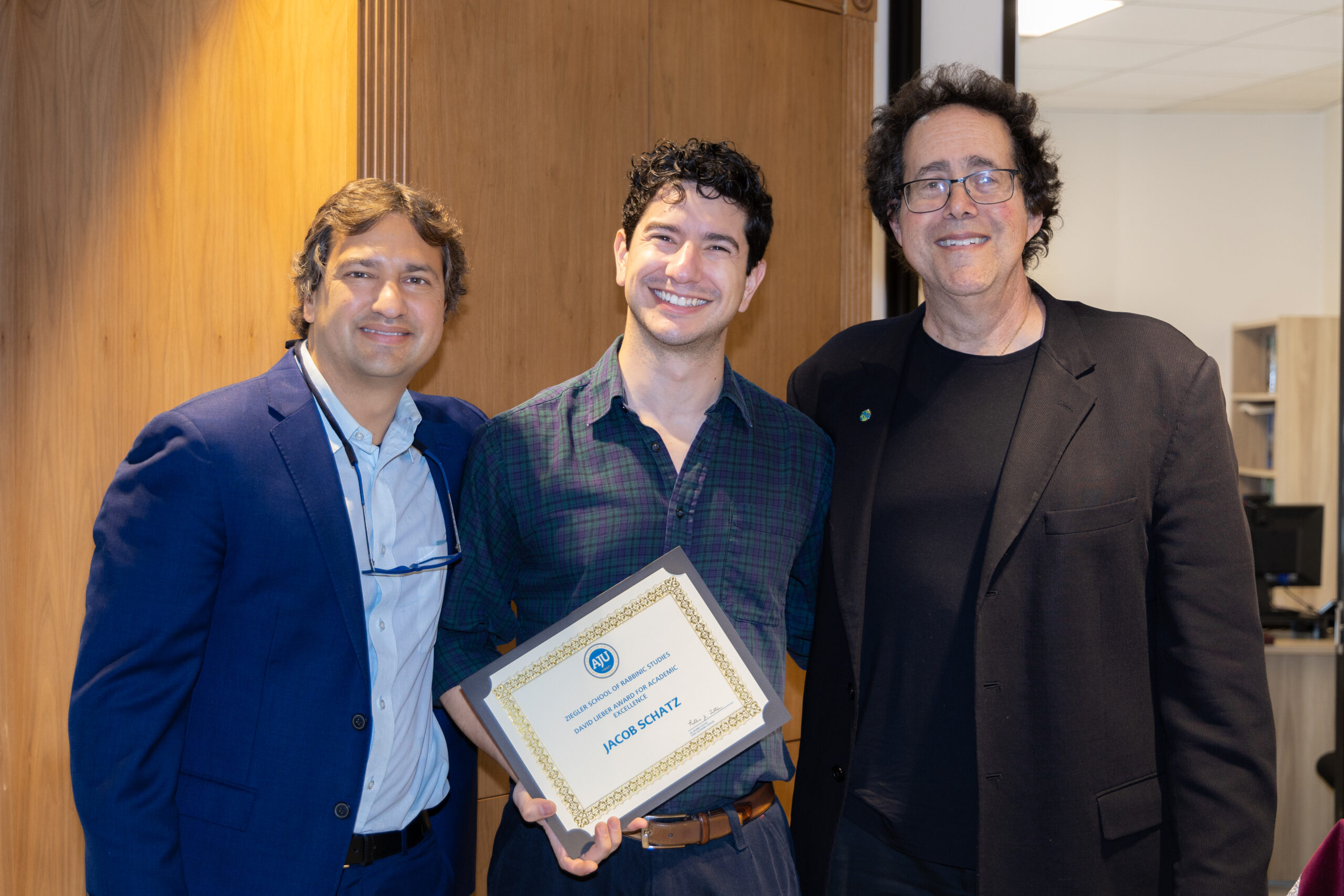 A Ziegler student smiles with a certificate for the David Lieber Award for Academic Excellence. The student is flanked by Ziegler rabbi